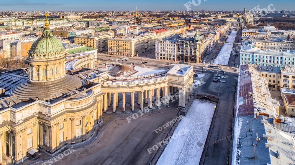 Фотография зимнего Санкт-Петербурга с высоты, открывающая вид на Казанский собор и Невский проспект, а также мосты и каналы исторического центра города. Панорамный ракурс позволяет оценить масштаб улиц, архитектурные детали зданий и гармоничное сочетание водных пространств с городской инфраструктурой. Снимок передает атмосферу зимнего Петербурга, его историческую архитектуру и уникальный облик северной столицы России. Изображение идеально подходит для туристических публикаций, коллекций фотографий, постеров и интерьерного оформления, а также для презентаций о городских достопримечательностях Петербурга.